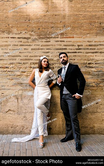 Young newly married couple standing against wall on footpath
