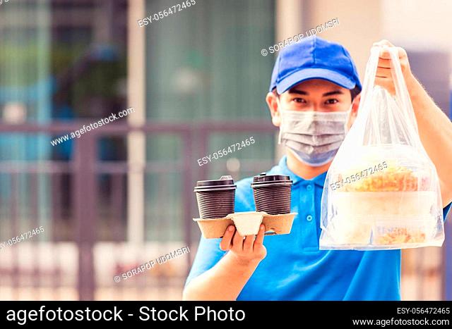 Asian young delivery man in blue uniform wearing face mask making grocery service giving rice food boxes plastic bags and coffee at front house under pandemic...