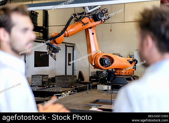 Businessmen standing against automated robotic arm machine at modern factory