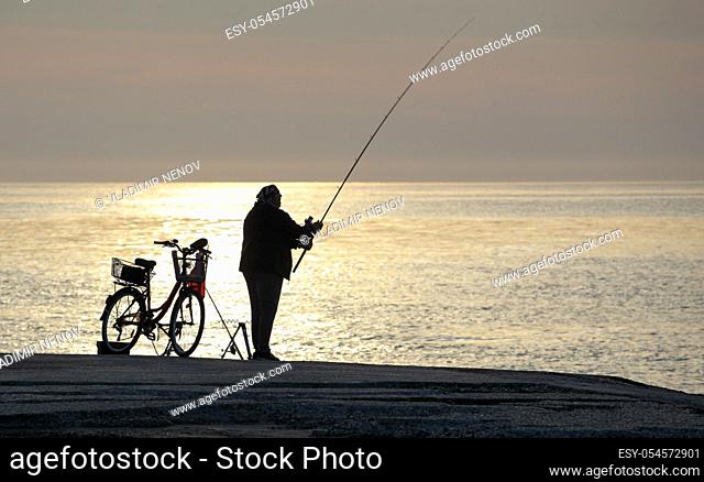 Pomorie, Bulgaria - May 11, 2020: A fisherman on the beach catches fish early in the morning