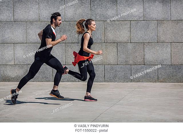 Side view of people jogging on sidewalk by wall