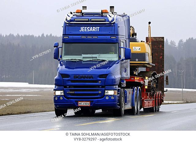 Jokioinen, Finland - March 23, 2019: Blue Scania R580 conventional cab of Maansiirto Jeesarit Oy hauls tracked excavator on trailer along highway
