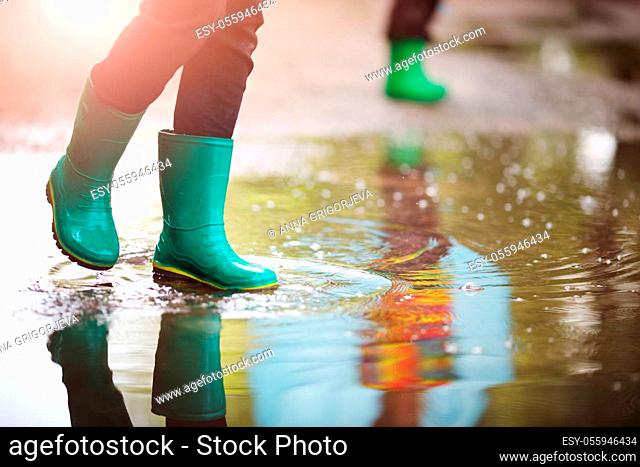 Child walking in wellies and jumping in puddle on rainy weather. Boy under rain in summer outdoors