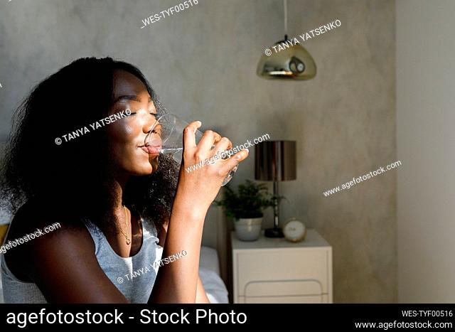 Woman with eyes closed drinking water in bedroom at home