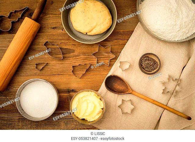 Flatlay collection of tools and ingredients for baking vegan Christmas cookies with margarine and chia seeds as egg replacement on a dark wooden table