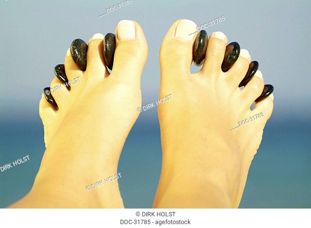 female feet with hot stone between the toes in front of blue background