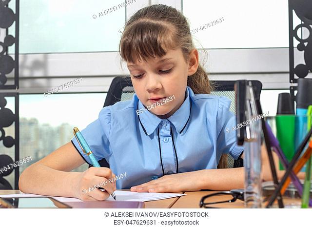 A girl of eight years old is concentrating writing with a fountain pen sitting at a table in an office