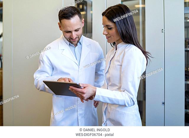 Colleagues with tablet wearing lab coats in modern factory