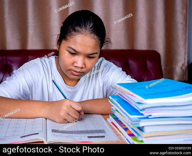 girl doing homework on a wooden table and there was a pile of books next to it The background is a red sofa and cream curtains