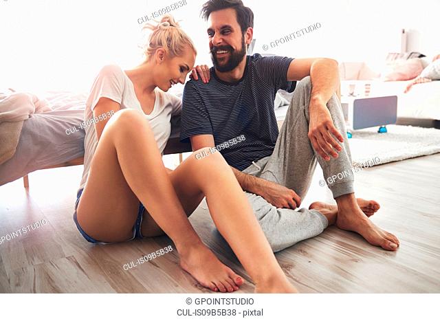 Couple sitting on floor beside bed, laughing