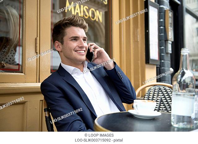 A man woman sitting outside a cafe on the phone in Covent Garden in London