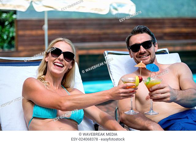 Couple sitting on sun lounger toasting cocktail