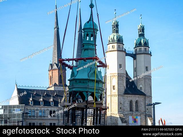 11 November 2021, Saxony-Anhalt, Halle (Saale): The spire of the town house in Halle/Saale hovers on the crane hook in front of the towers of the town church...