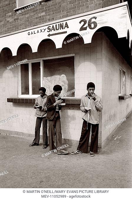 Boys eat chips beneath a sign for a Salford sauna