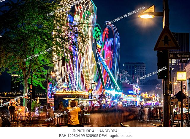 03 August 2019, Hessen, Frankfurt/Main: During the Mainfest, a carousel leaves its traces of light above the stream of visitors passing by