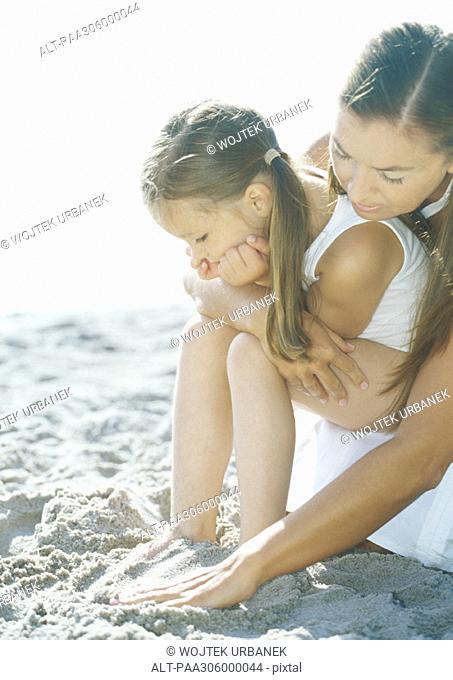 Girl sitting on mother's lap on beach