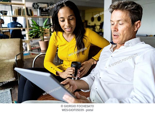 Businesswoman and businessman sharing tablet on sofa in loft office