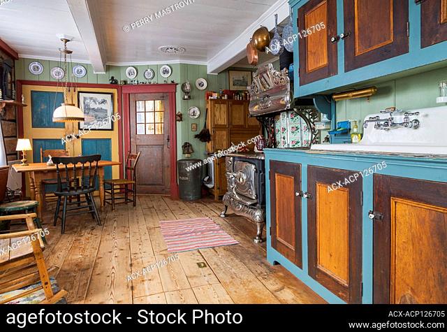 Pinewood with linden wood cabinets, antique 1915 Belanger Royal wood-burning cooking stove and dining table with assorted chairs in kitchen with worn wide...