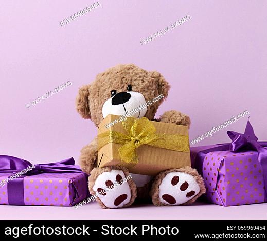 cute brown teddy bear and box wrapped in paper and silk ribbon on a purple background. Prize and congratulations