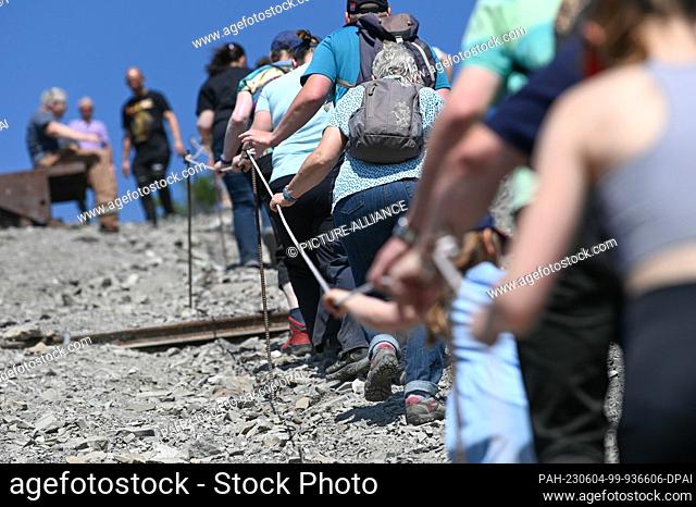 04 June 2023, Saxony-Anhalt, Volkstedt: Visitors climb the tailings pile along a rope. The dump is part of the former ""Fortschritt"" copper mining shaft near...
