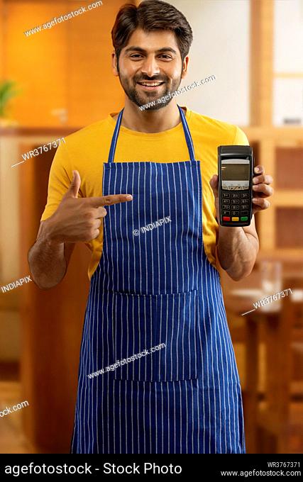 A HAPPY WAITER POINTING TOWARDS CARD MACHINE WHILE WORKING AT RESTAURANT