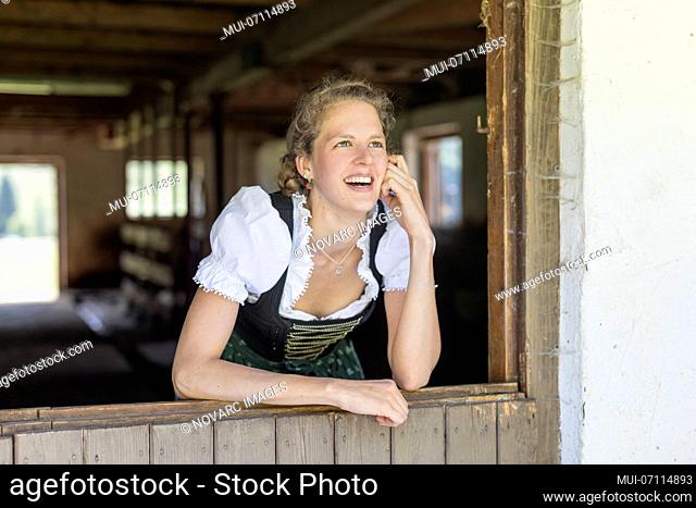 Farmer with dirndl looks out of the stable door