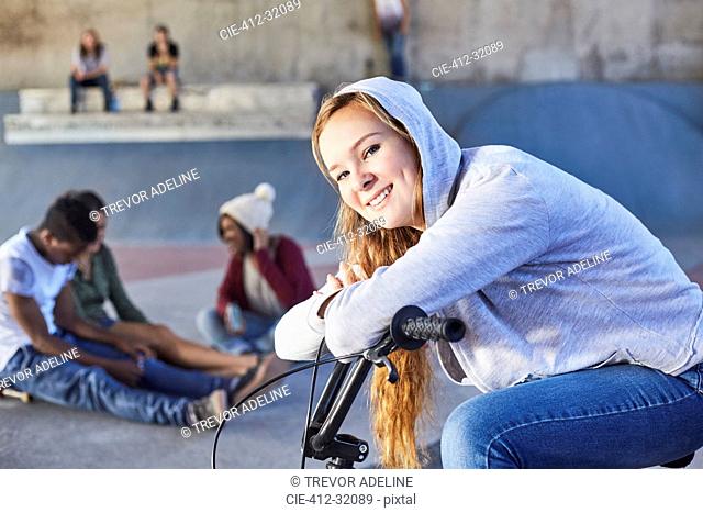 Portrait smiling teenage girl leaning on BMX bicycle at skate park