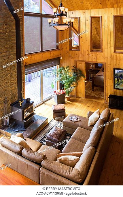 Toip view of tan leather sectional sofa and wood burning stove in living room area of the great room with cathedral ceiling inside a milled cottage style flat...