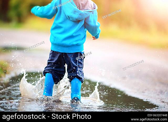 Small child jumping through puddles in nature in spring. Concept of the childhood and family relation
