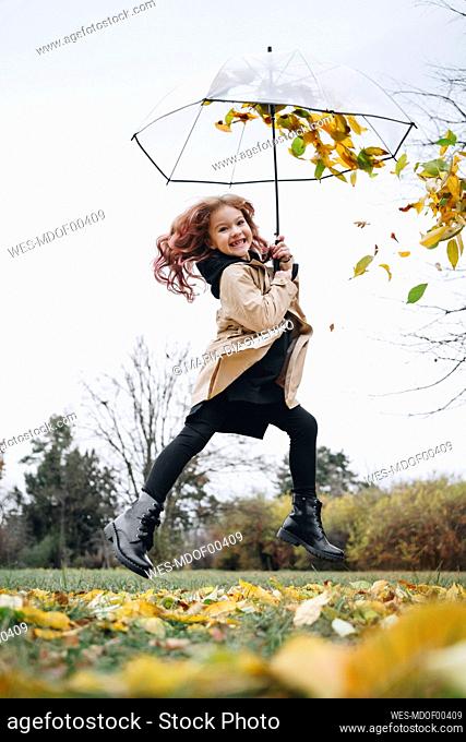 Cheerful cute girl jumping with umbrella in park