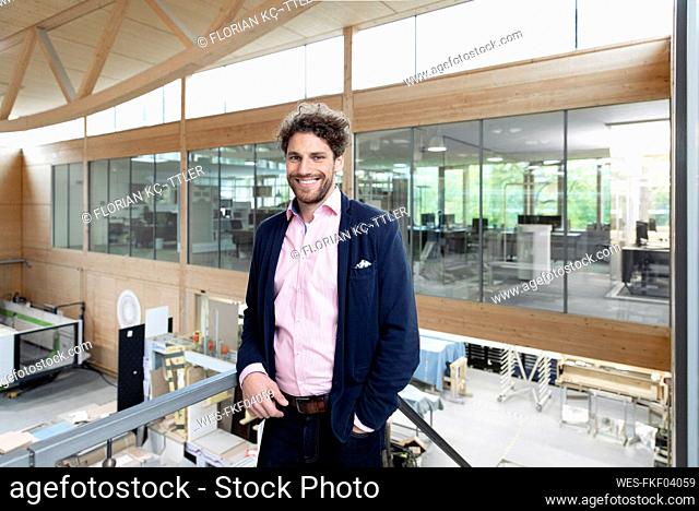 Smiling male entrepreneur leaning on railing in factory