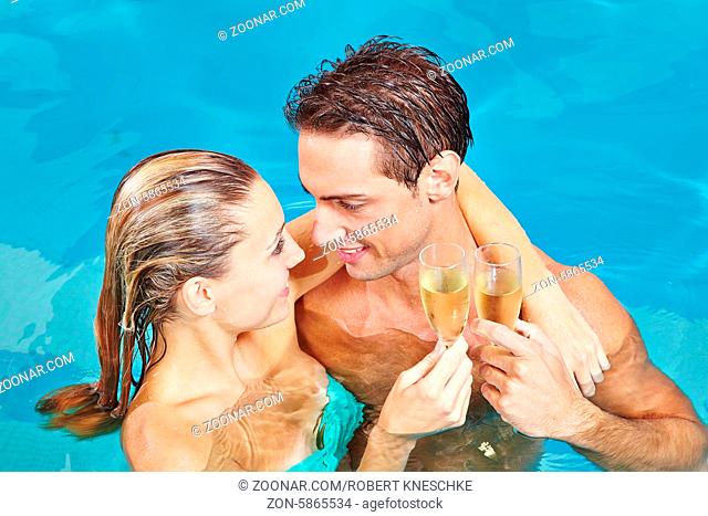 Glückliches Paar im Pool stößt an mit einem Glas Champagner