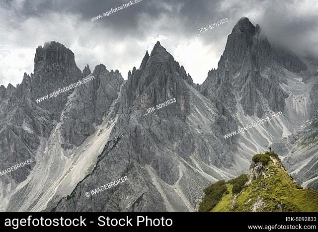 Woman standing on a ridge, behind mountain tops, rocky ridge with sharp rocky peaks, dramatic clouds, Cimon di Croda Liscia and Cadini group, Sesto Dolomites