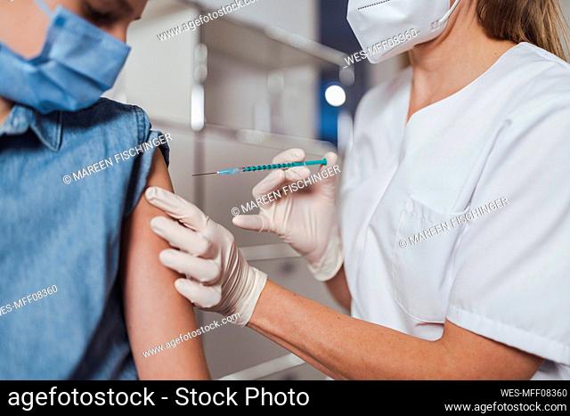 Doctor administering boy with COVID-19 vaccine at vaccination center