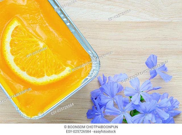 Orange soft cake with sliced orange fruit in aluminum foil tray on wooden background