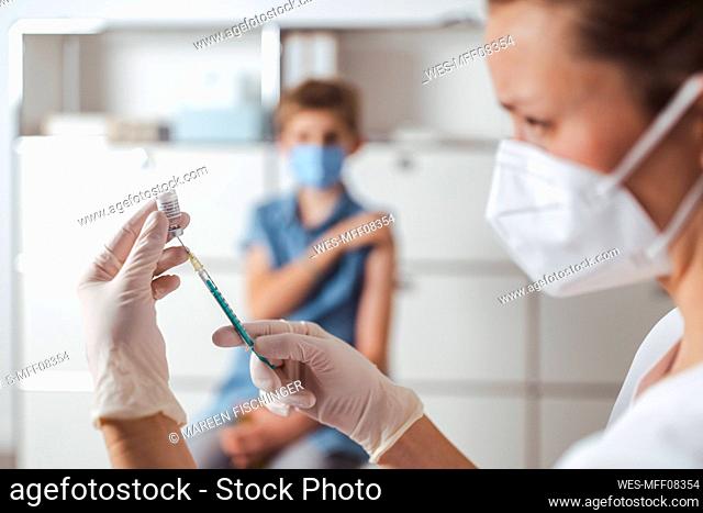 Nurse preparing COVID-19 vaccine with boy in background at center