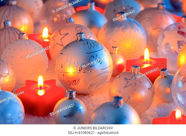 Silver Christmas baubles and burning small, star shaped candles. Studio picture. Switzerland