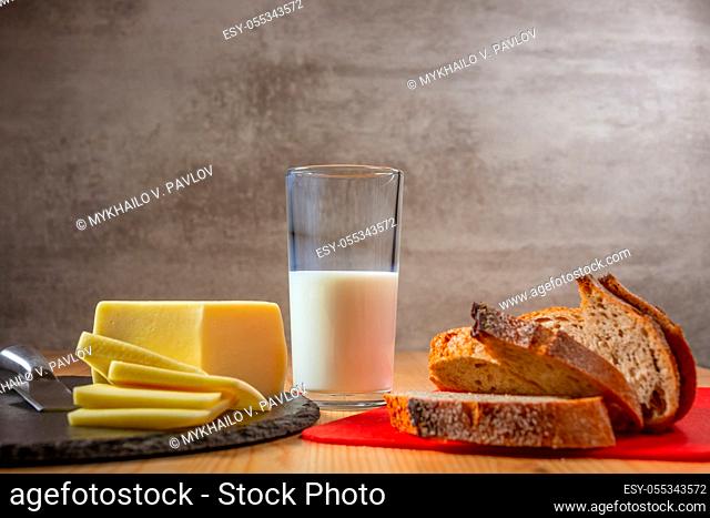Slices of fresh cheese and bread on a wooden table. Glass of milk. Organic food
