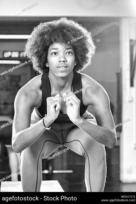 Fit young african american woman box jumping at a crossfit style gym. Female athlete is performing box jumps at gym