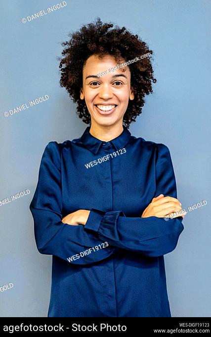 Happy businesswoman with arms crossed standing against blue background