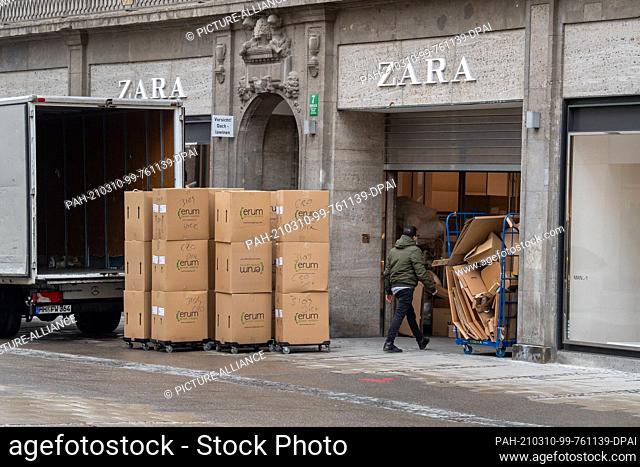 10 March 2021, Bavaria, Munich: A shop with a half-closed roller shutter in the city centre is supplied with goods in the morning hours