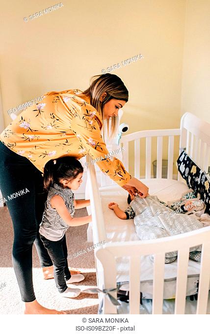Girl and mother putting baby brother in crib