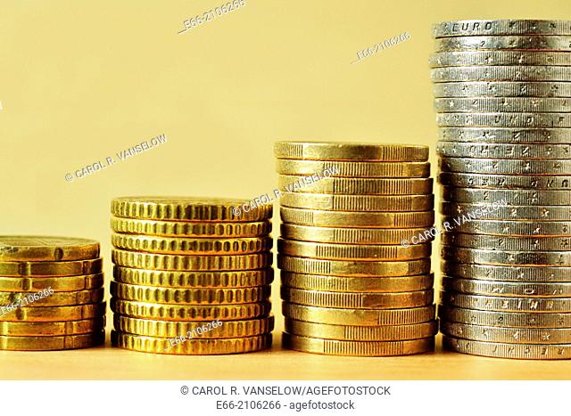 Stacks of euro coins against a light background. Coins are arranged by denomination, showing a upward trend
