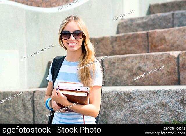 Smiling college student sitting on staircase and studying with books