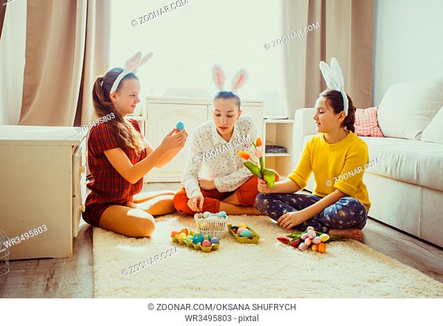 Girlfriends in bunny ears sitting on the floor and playing with Easter rabbit. The concept of preparation for Holiday