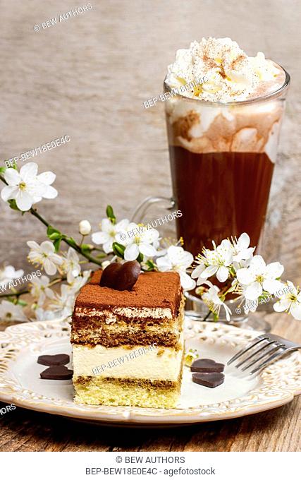 Tiramisu cake on white plate. Blossom apple branch and cup of irish coffee in the background