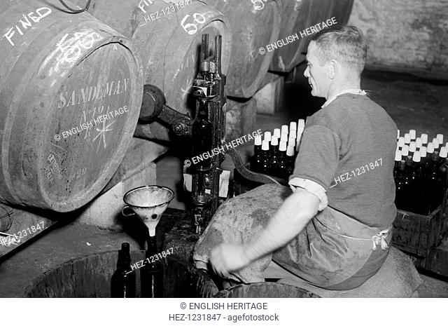 Port wine being bottled from the barrel at the Cutler Street warehouses, London, c1945-c1965. The barrels are stamped 'Sandeman'