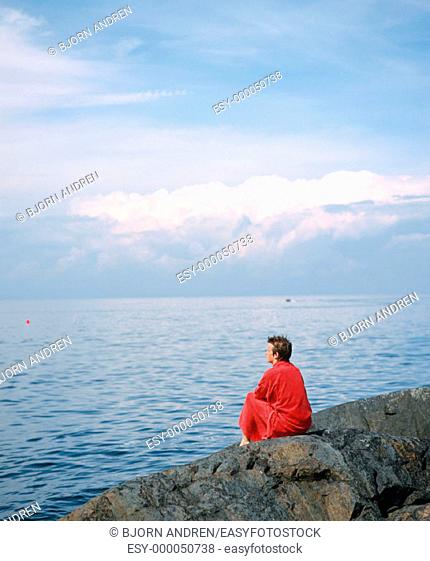 Boy looking at sea with bathrobe. Landsort Island. Sweden