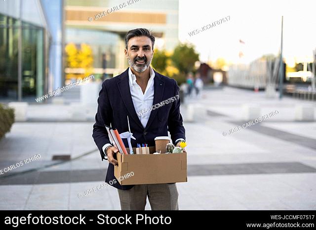 Smiling businessman holding box with office supplies