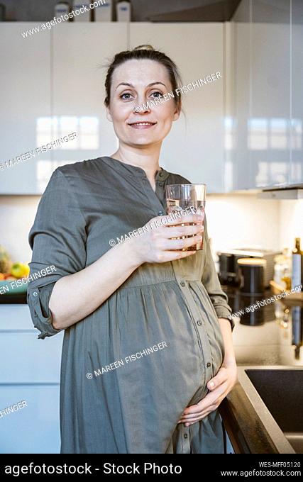 Portrait of pregnant woman holding glass of water in kitchen at home